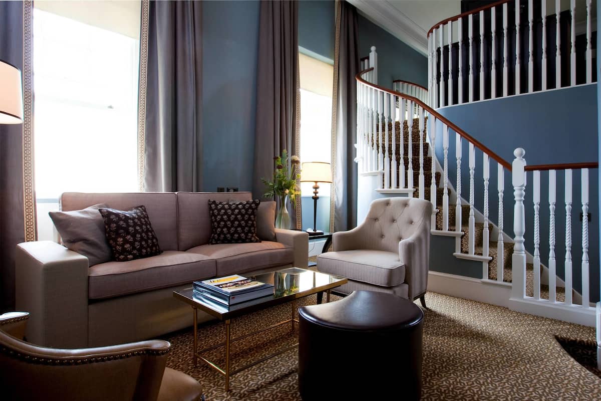 Ein Wohnzimmer mit einer Couch, einem Sessel, einem Couchtisch und einer Treppe mit weißen Balustraden.
