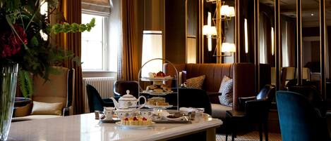 A hotel room with a dining table set for tea, a sofa, and a mirror with lights.