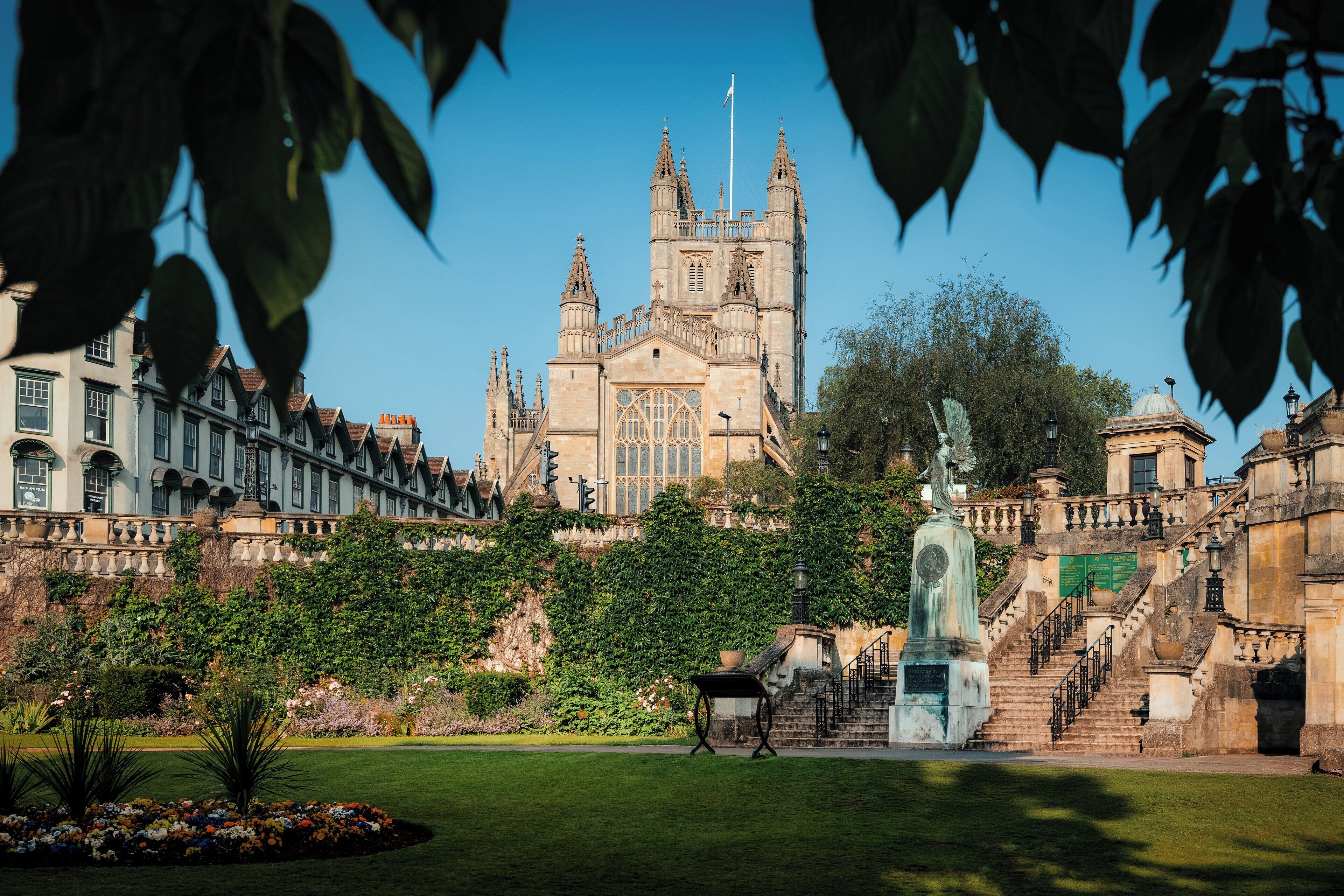 A historic building with a large central tower, surrounded by lush gardens and a statue.