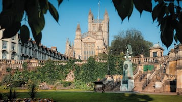 A historic building with a large central tower, surrounded by lush gardens and a statue.