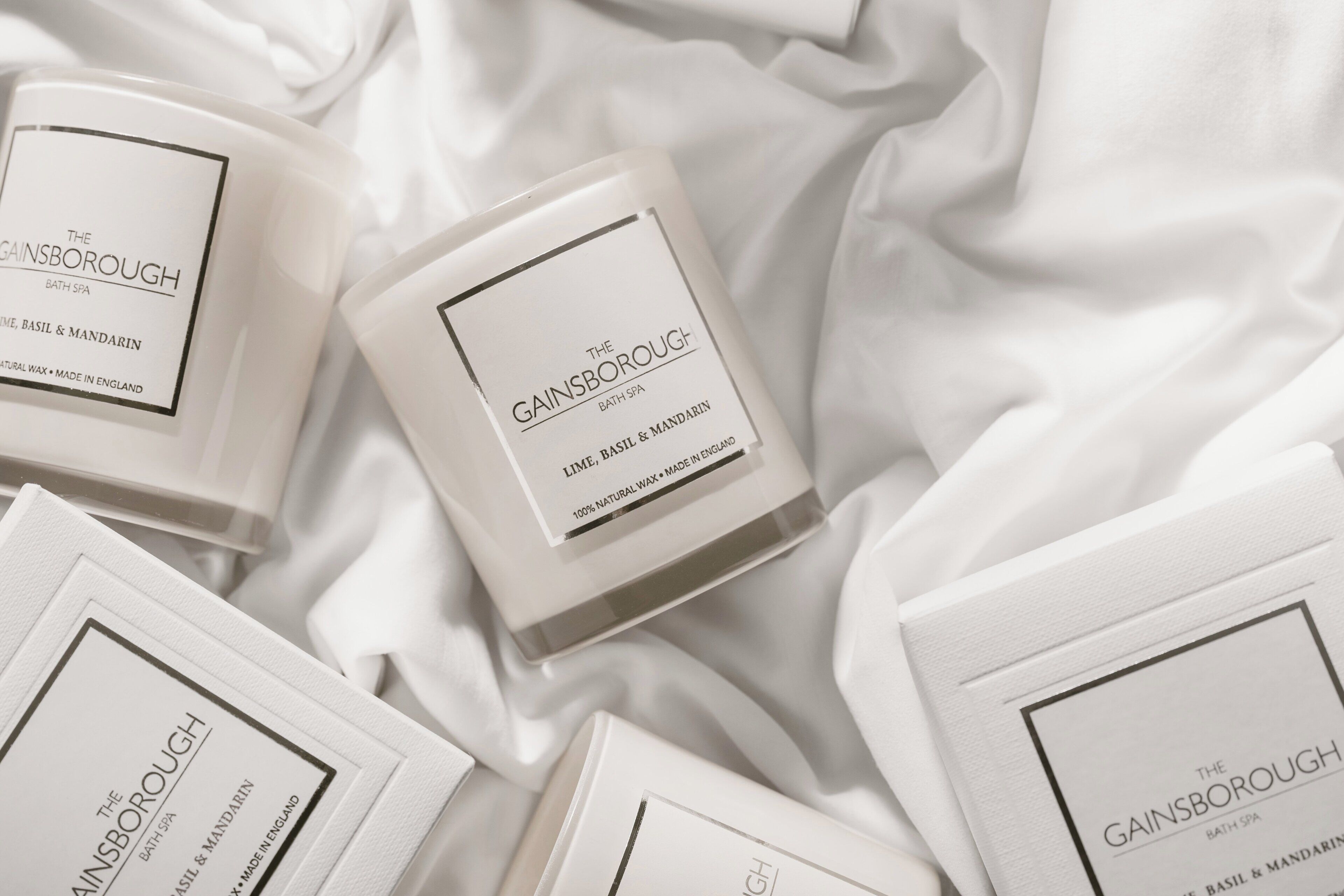 Several white candles with labels from The Gainsborough Bath Spa, featuring natural wax and made in England.