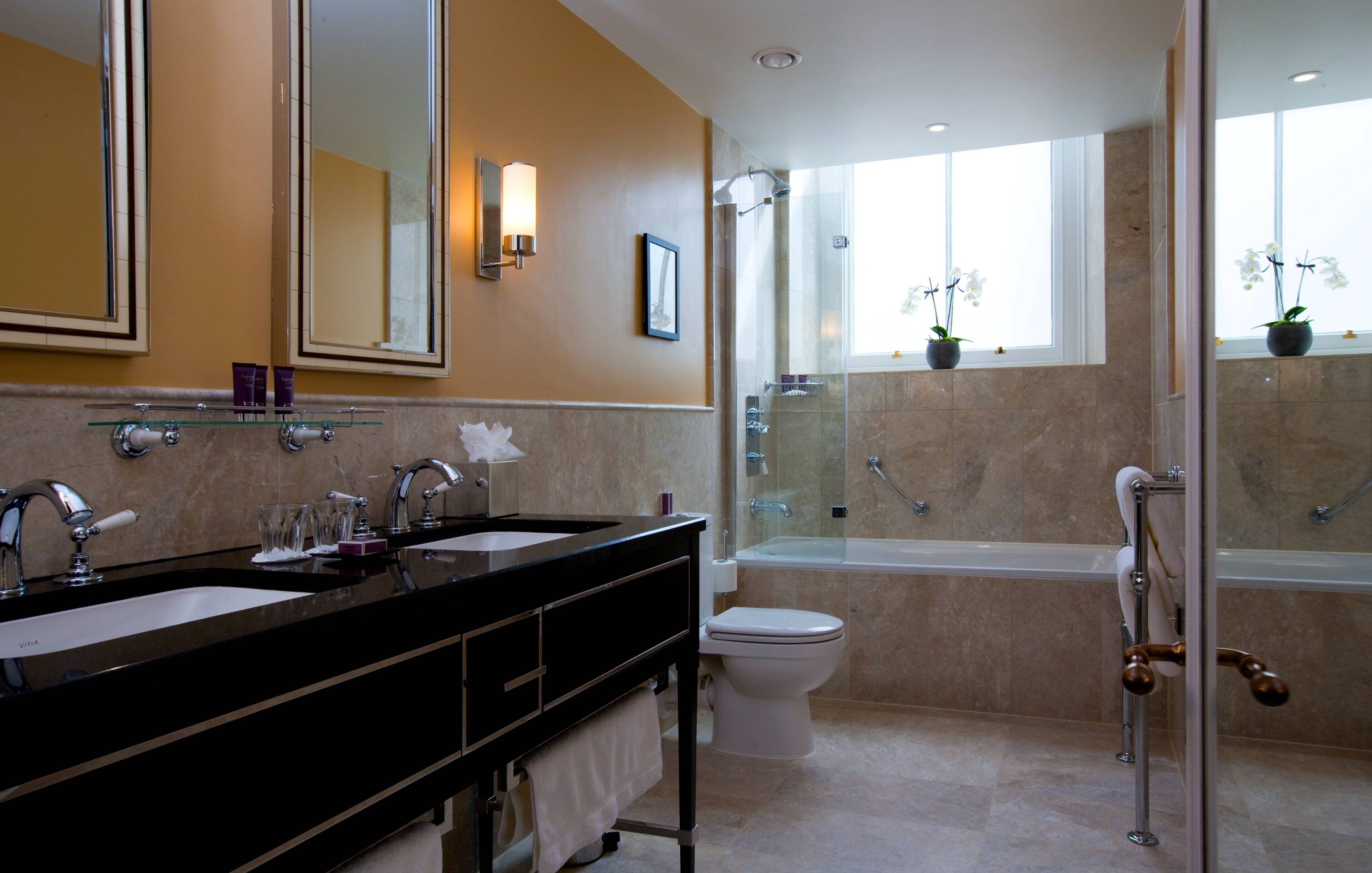 Une salle de bain moderne dotée d’un meuble-lavabo à deux vasques, de toilettes, d’une baignoire et d’une douche à parois de verre.