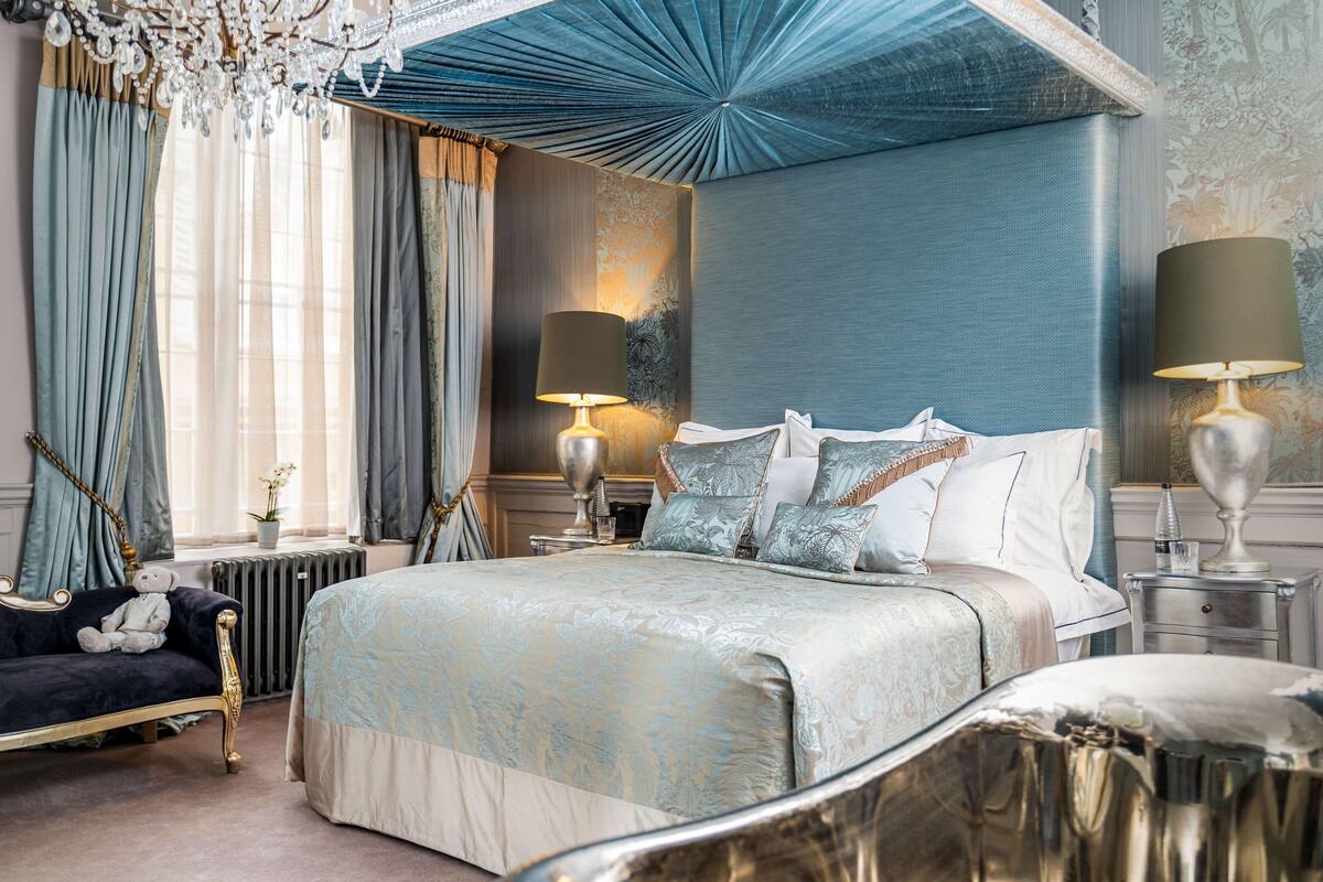 Ein Schlafzimmer mit einem großen Bett, zwei Nachttischen, einem Schminktisch und einem gemütlichen Sessel, sowie einer Kristallleuchtre.