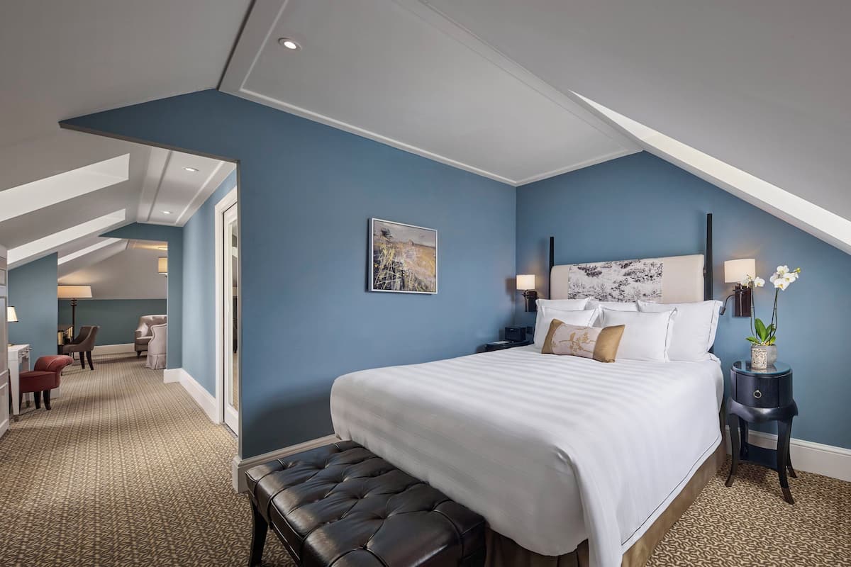 Ein Hotelzimmer mit einem großen Bett, einer Bank, einem Nachttisch und einem Schreibtisch mit Stuhl.