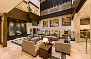 A spacious lobby with multiple seating areas, a central decorative wall, and a modern staircase.