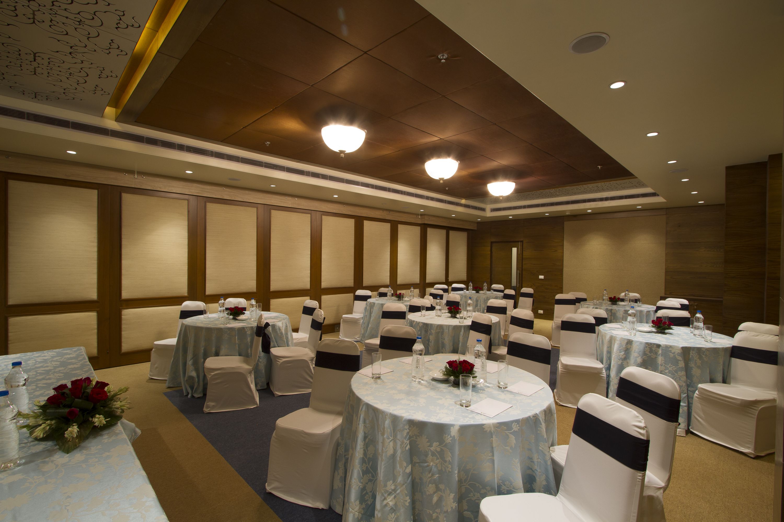 A banquet hall with round tables, white chairs, and blue tablecloths.