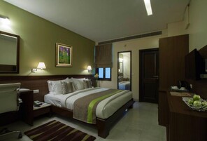 Quarto de hotel com cama, mesas de cabeceira, escrivaninha e uma cadeira, espelho e janela com cortinas.