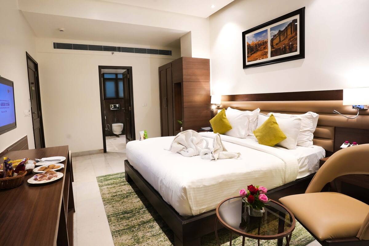 A hotel room with a bed, a desk with breakfast items, a chair, and a small table with flowers.