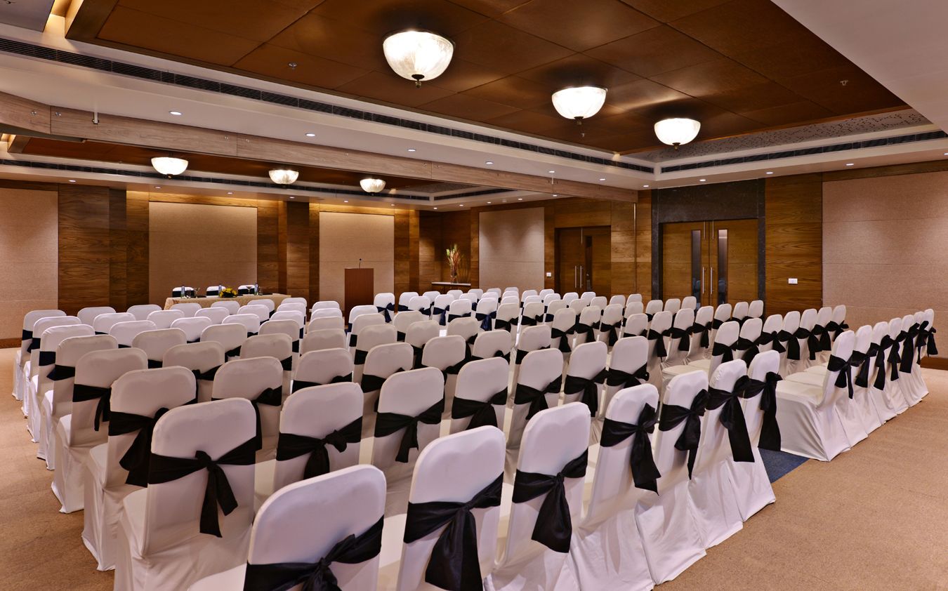 A conference room with rows of white chairs with black sashes, a podium, and a large screen.