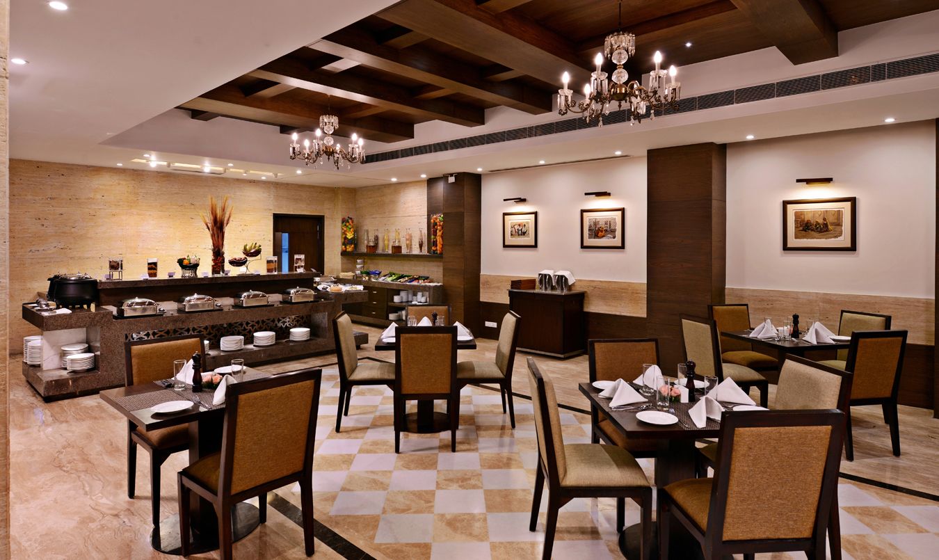 Un restaurante con suelo a cuadros, vigas de madera y candelabros. Las mesas están preparadas con platos y vasos.