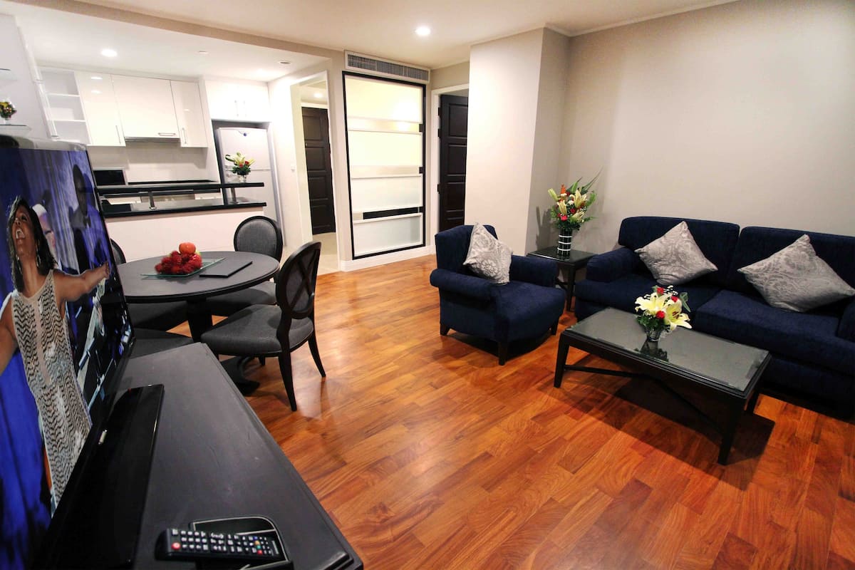A modern living room with a dark blue sofa set, a coffee table with a vase of flowers, and a dining area with a table and chairs.