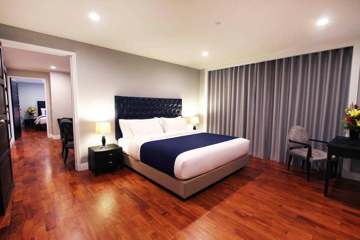 A hotel room with a large bed, bedside tables, a desk with a chair, and a view of a curtain-covered window.