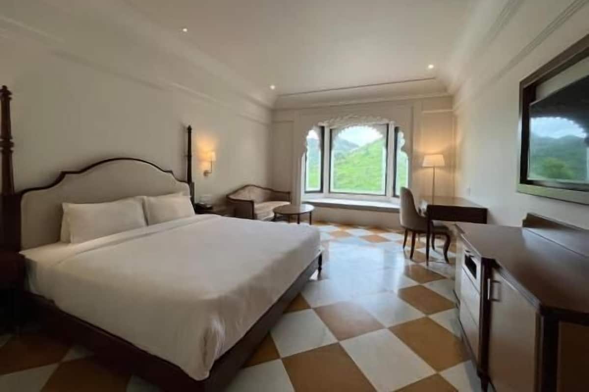 A hotel room with a large bed, a desk, a chair, a window with a view, and a lamp.