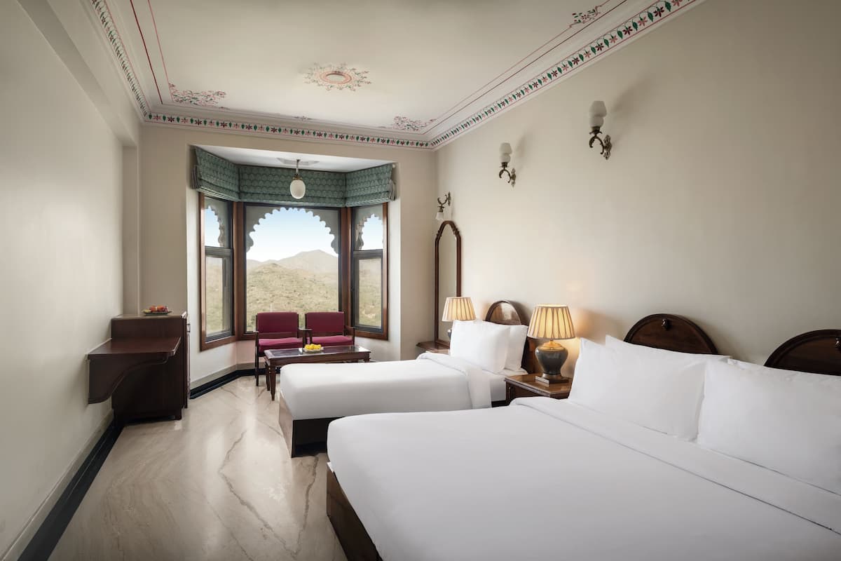 A hotel room with two beds, a desk, a chair, and a view of the desert.