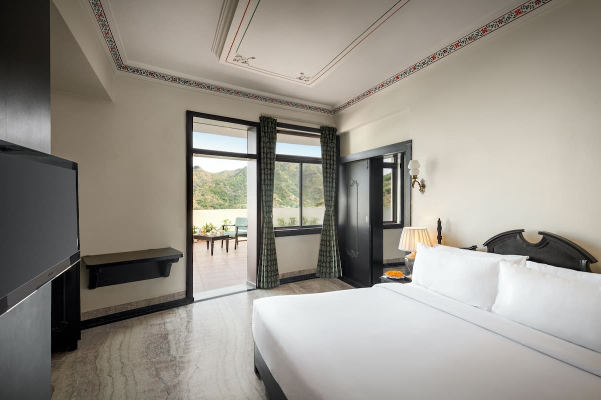A hotel room with a bed, a TV, a desk, and a window with curtains.