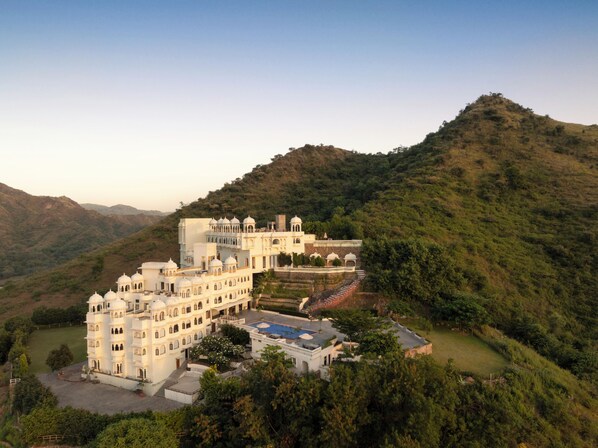 A large, multi-story building with a courtyard, surrounded by lush green hills. - Bhairavgarh Palace Udaipur (Udaipur)