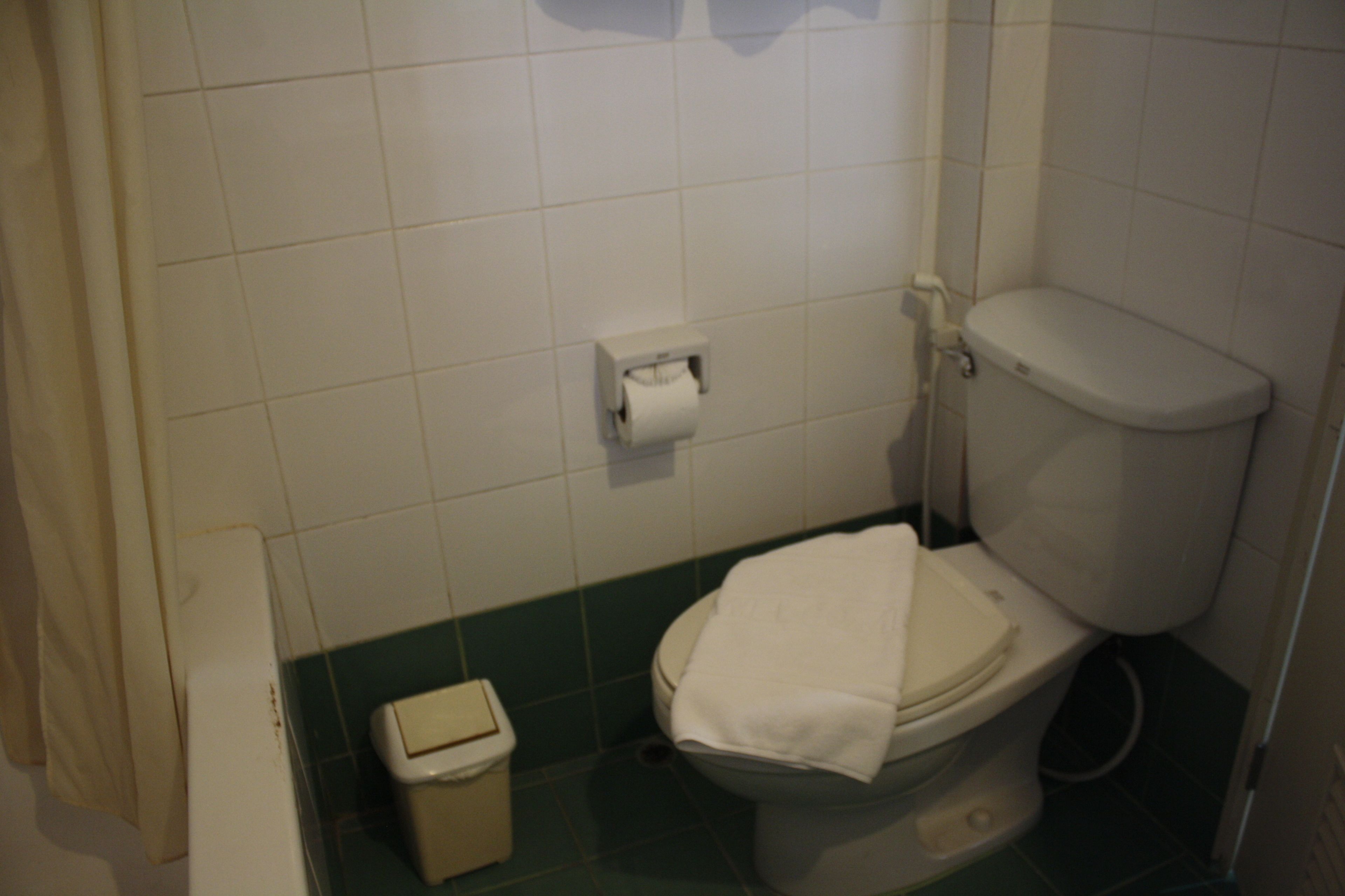 A small bathroom with a toilet, a paper towel dispenser, and a trash bin.