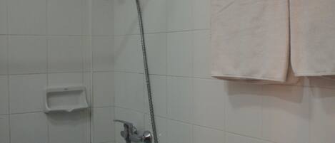 Un baño con paredes de azulejos blancos, cabina de ducha de vidrio, inodoro y toallero con dos toallas.