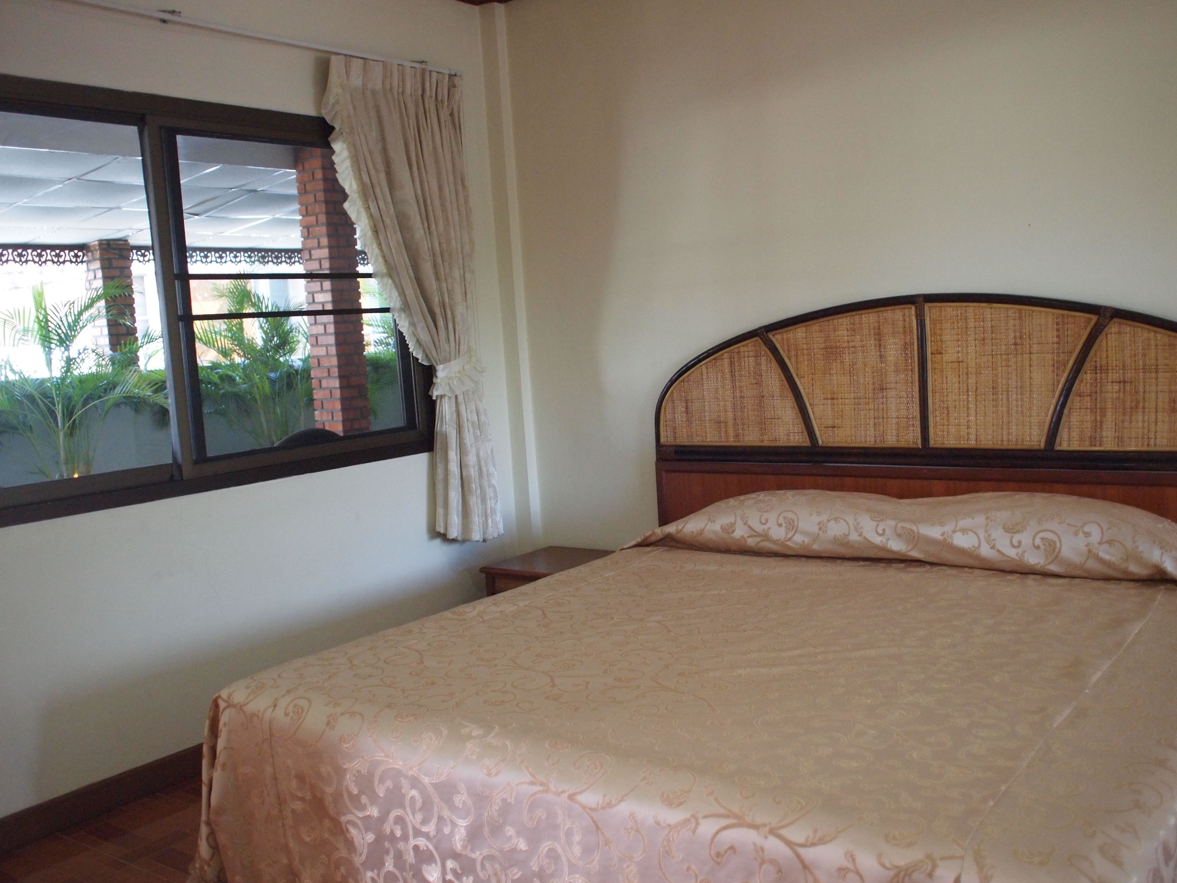 A bedroom with a bed, a window with curtains, and a view of greenery outside.