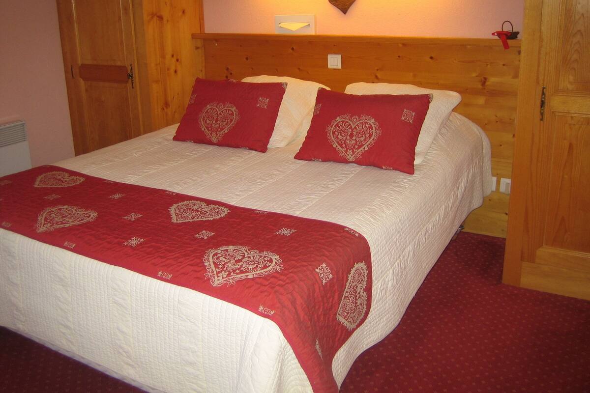 Une chambre à coucher avec un cadre en bois, un lit, des oreillers à motifs de cœurs rouges et une couvre-lit rouge.