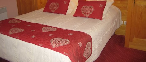 A wooden-framed bedroom with a bed, red heart-patterned pillows, and a red bedspread.