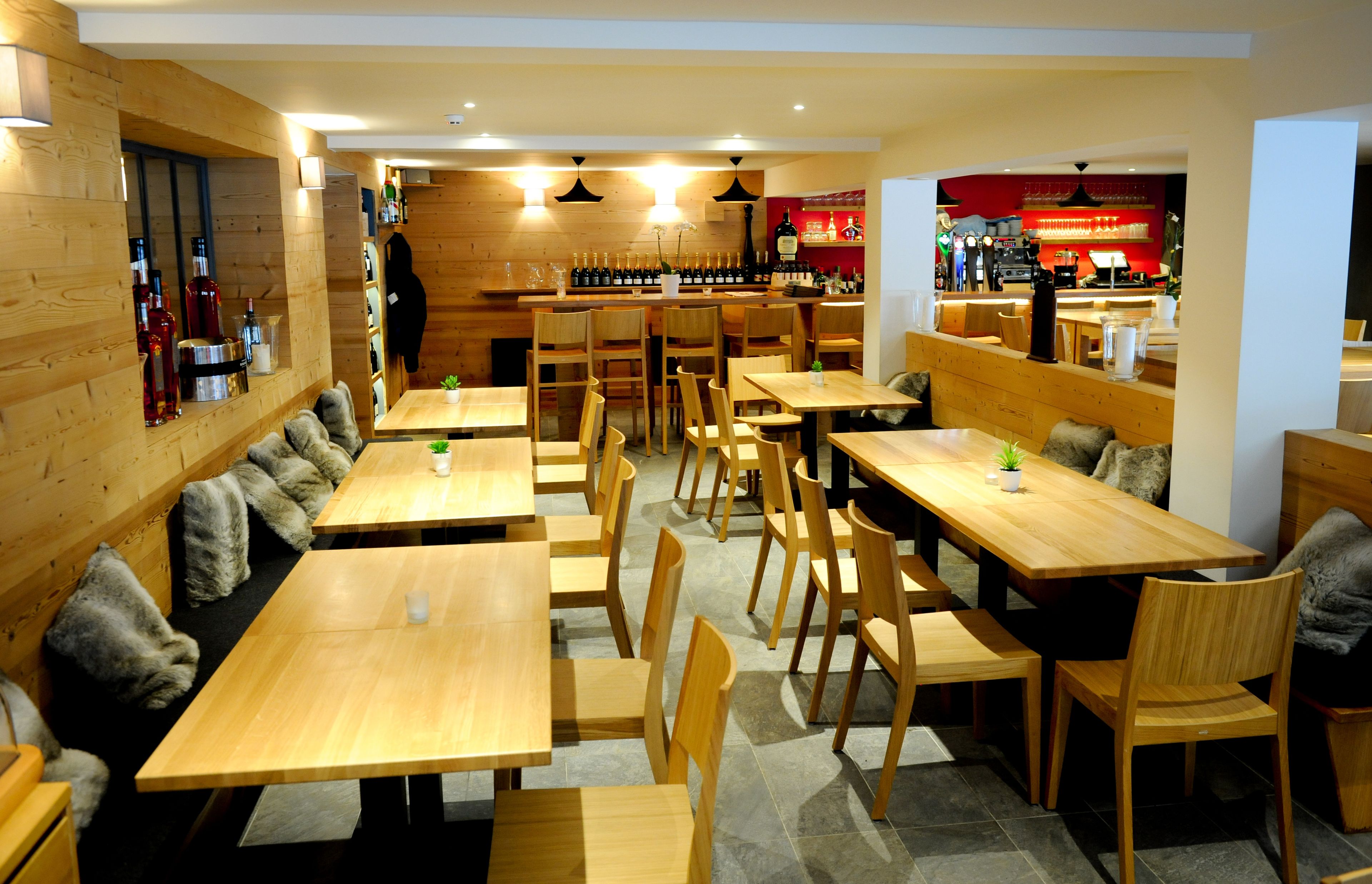 A restaurant with wooden tables and chairs, a bar area, and a seating section with cushioned benches.