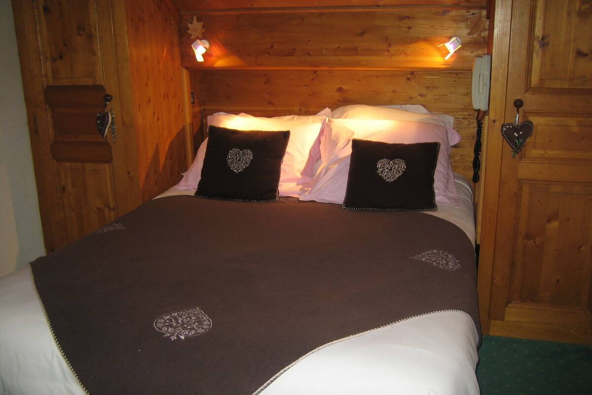 Une pièce en bois avec un lit, deux oreillers en forme de cœur, un téléphone sur la table de chevet et un luminaire fixé au mur.