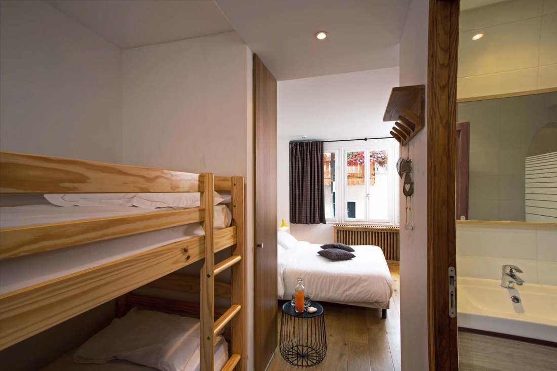 Una habitación con literas, una cama individual, una mesita con una botella y un baño con bañera.