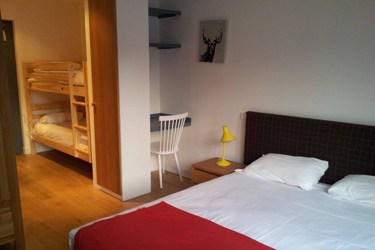 Une chambre avec un lit superposé, un bureau avec une chaise, une table de chevet avec une lampe et un lit avec des oreillers.