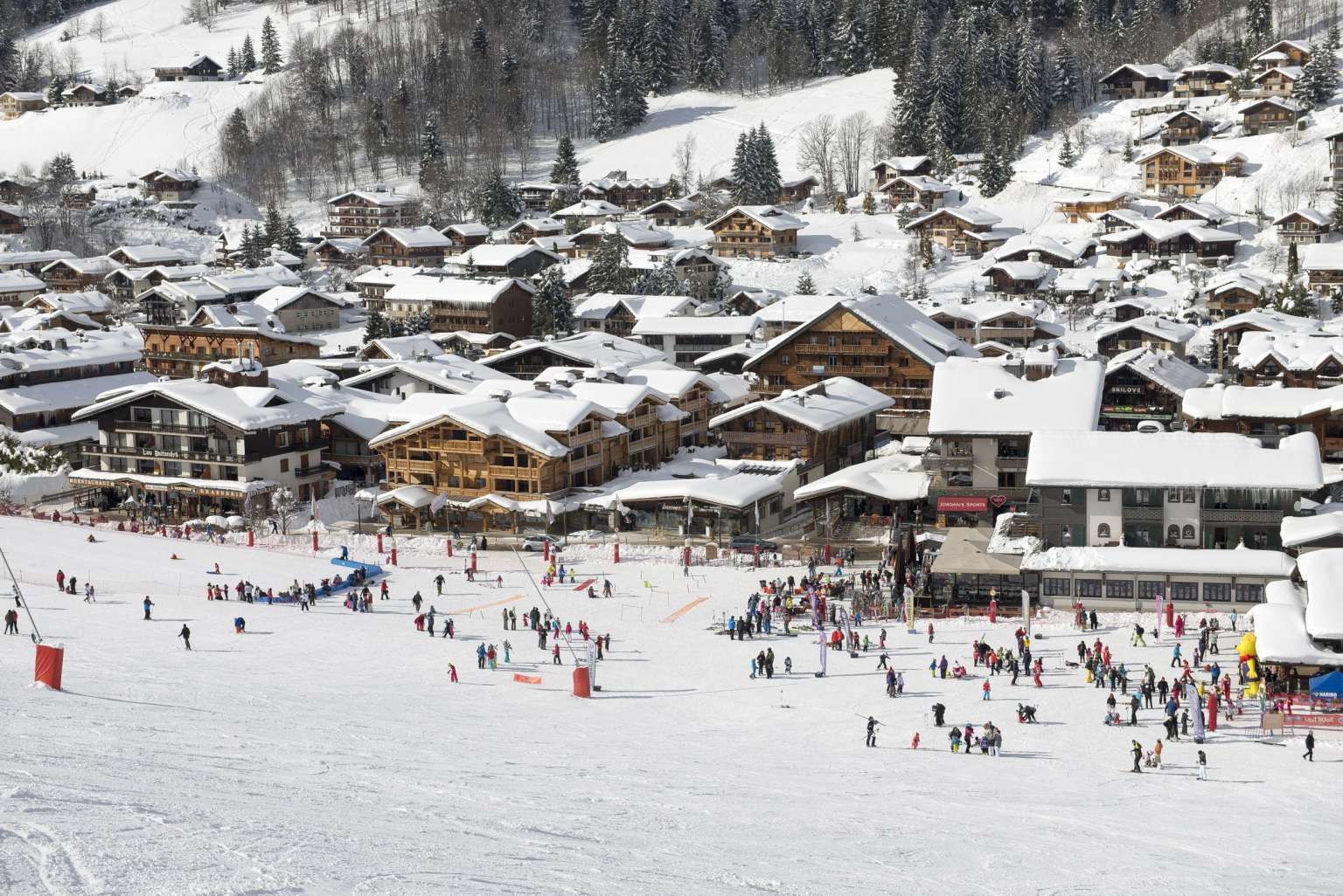 A snow-covered ski resort with multiple wooden lodges and a ski slope.