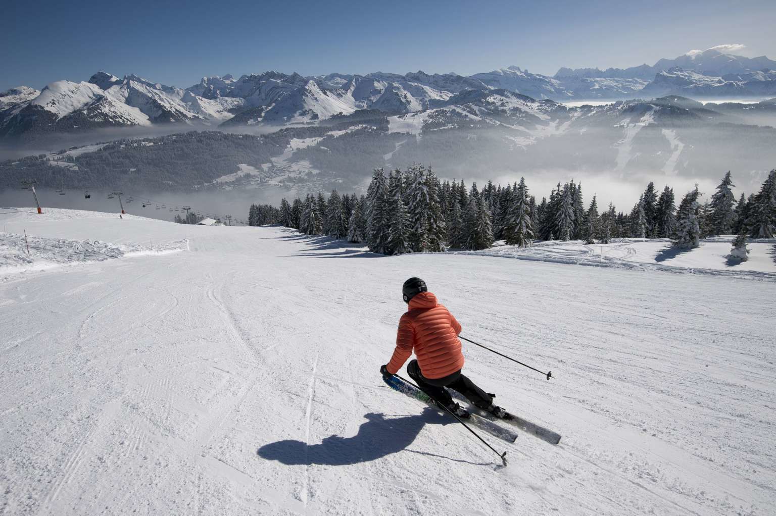 Una persona esquiando por una pendiente nevada, con montañas al fondo.