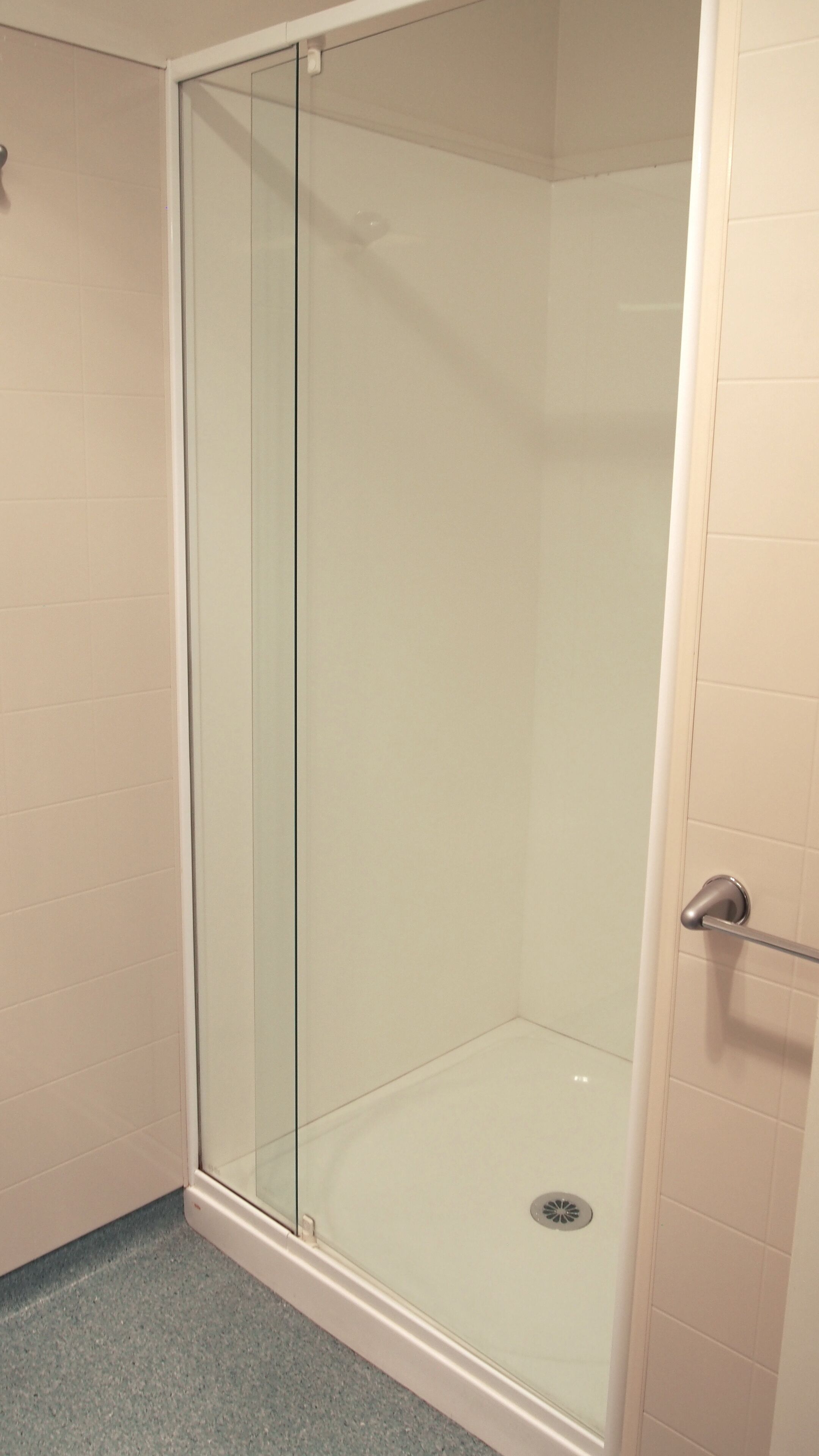Cabina de ducha con paredes de vidrio, un grifo metálico y desagüe.
