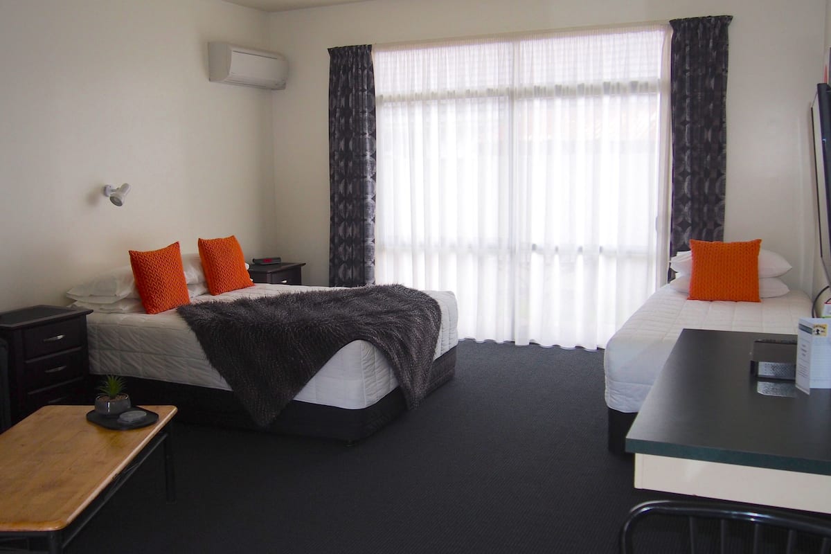 A hotel room with a bed, a desk, a chair, a small table, and a TV.