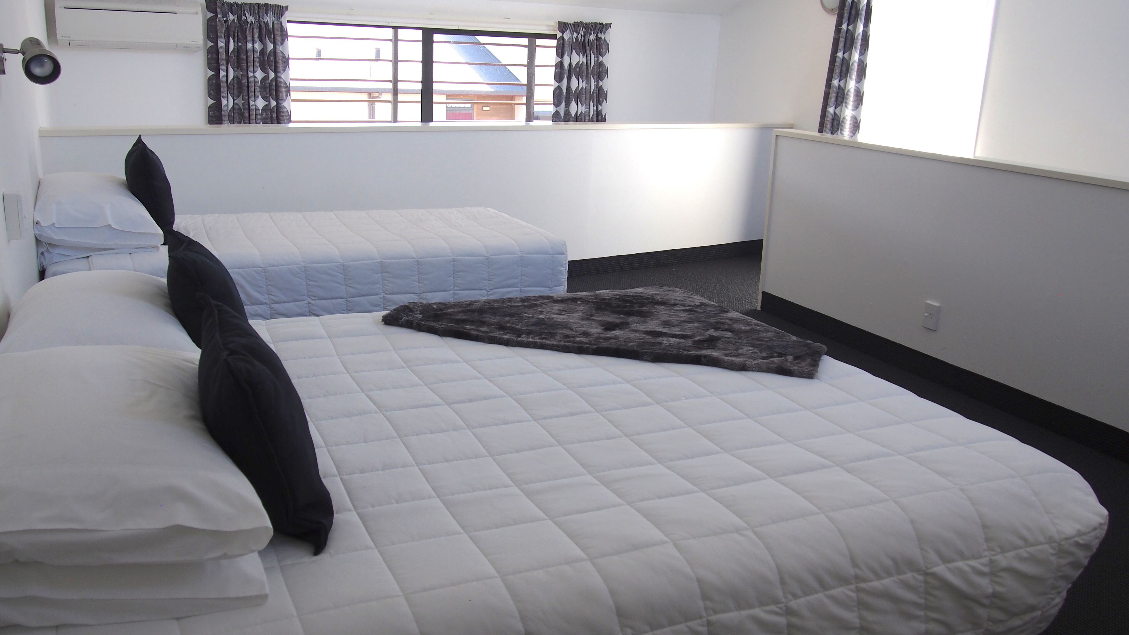 Een hotelkamer met twee bedden, een raam met gordijnen, een radiator en een wandairconditioner.