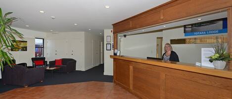 A reception area with a wooden desk, a receptionist, and a Totara Lodge sign.