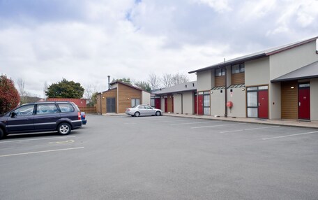 A parking lot with two cars, a building with multiple doors, and a clear sky.