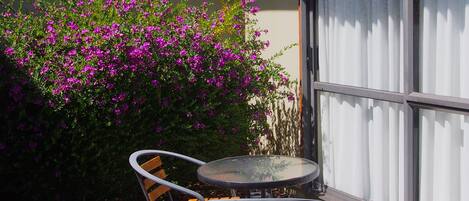 An outdoor patio with a round table and two chairs, surrounded by vibrant purple flowers.