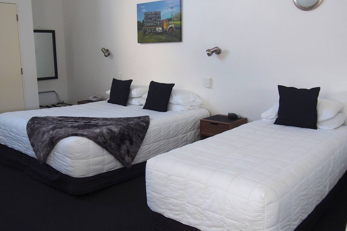 A hotel room with two beds, a painting on the wall, and a small wooden nightstand with a phone and a cup.