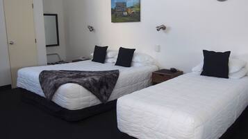 A hotel room with two beds, a painting on the wall, and a small wooden nightstand with a phone and a cup.