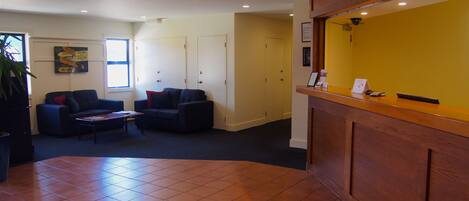 A reception area with a wooden reception desk, two sofas, a coffee table, and a tiled floor.