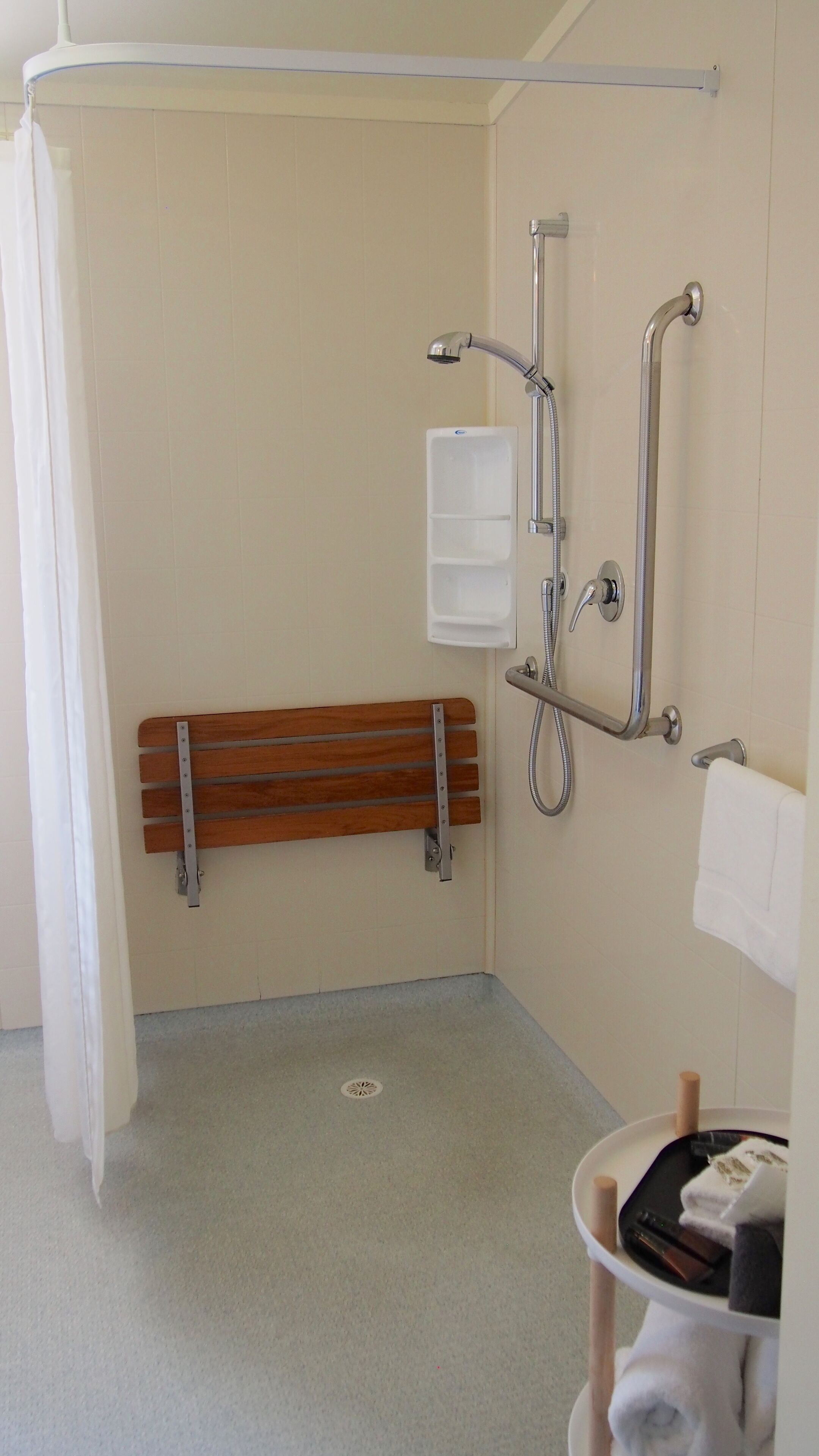 Un baño pequeño con ducha, un banco, toallero y un inodoro.