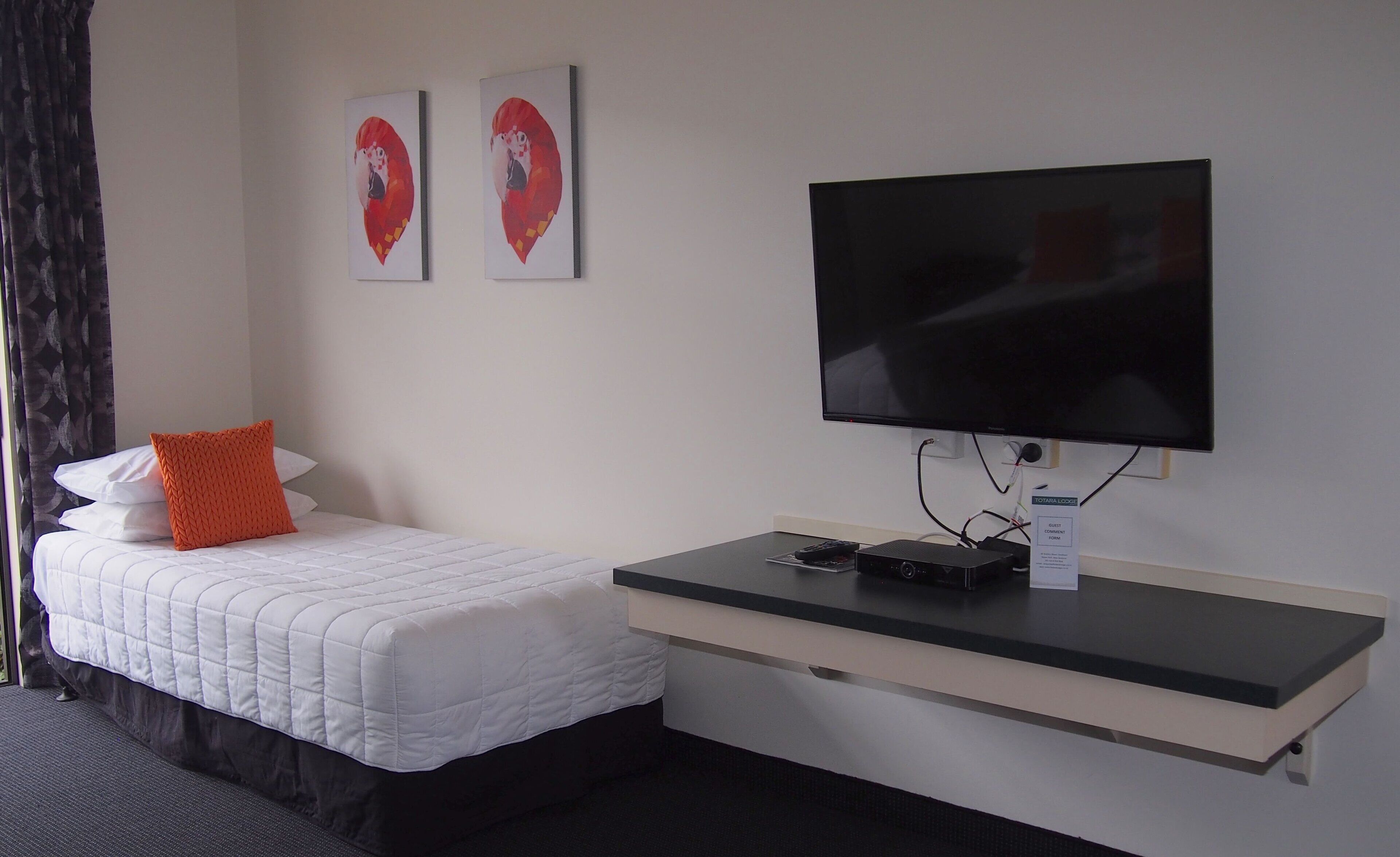A hotel room with a bed, a TV, a desk, and two framed artworks on the wall.