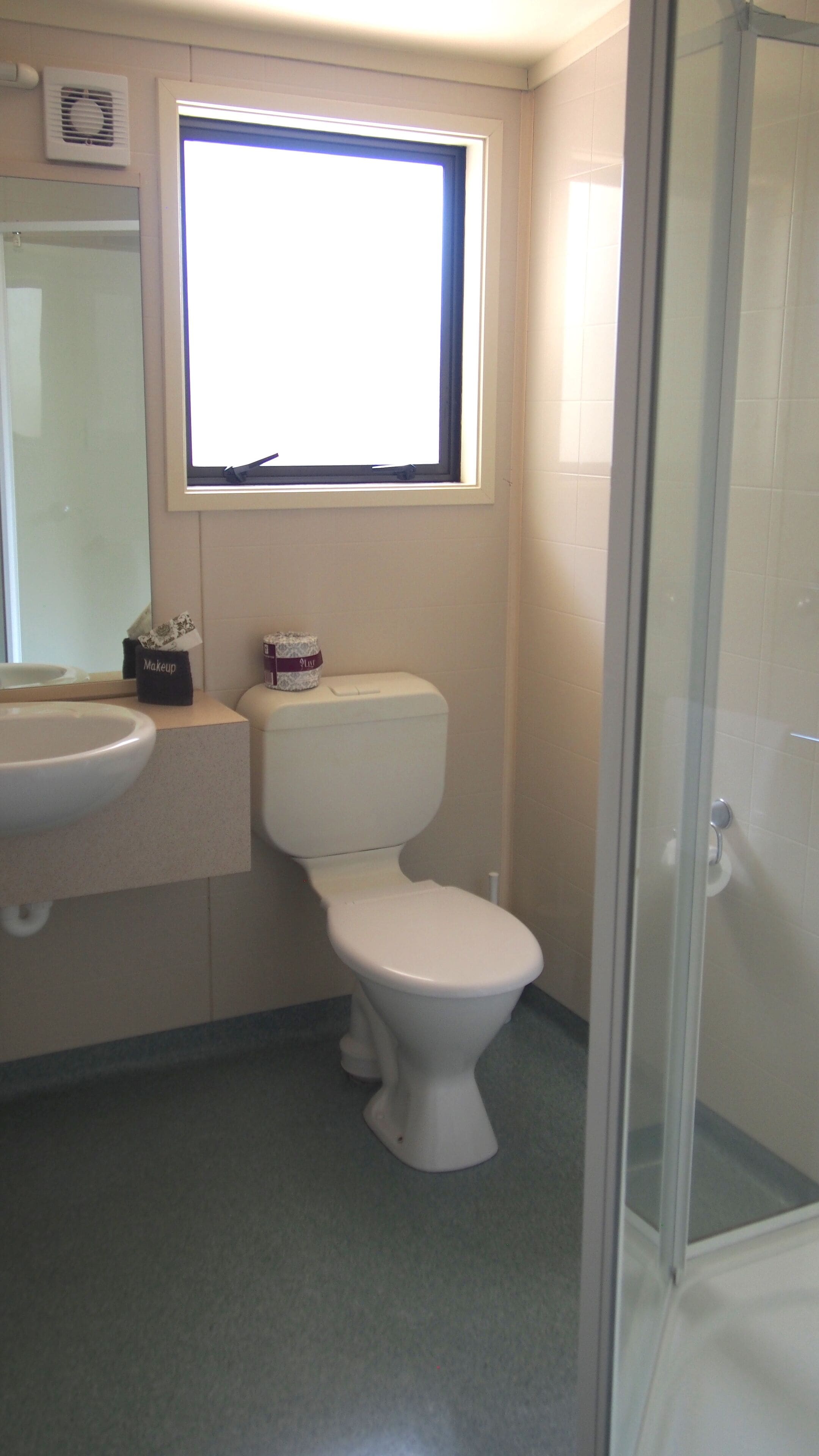 A bathroom with a toilet, a sink, a window, and a shower.