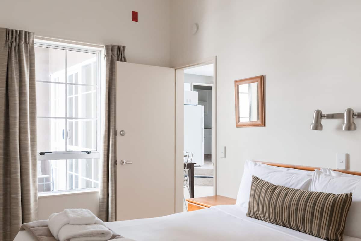 A hotel room with a large bed, a bedside table, a mirror, and a window with curtains.