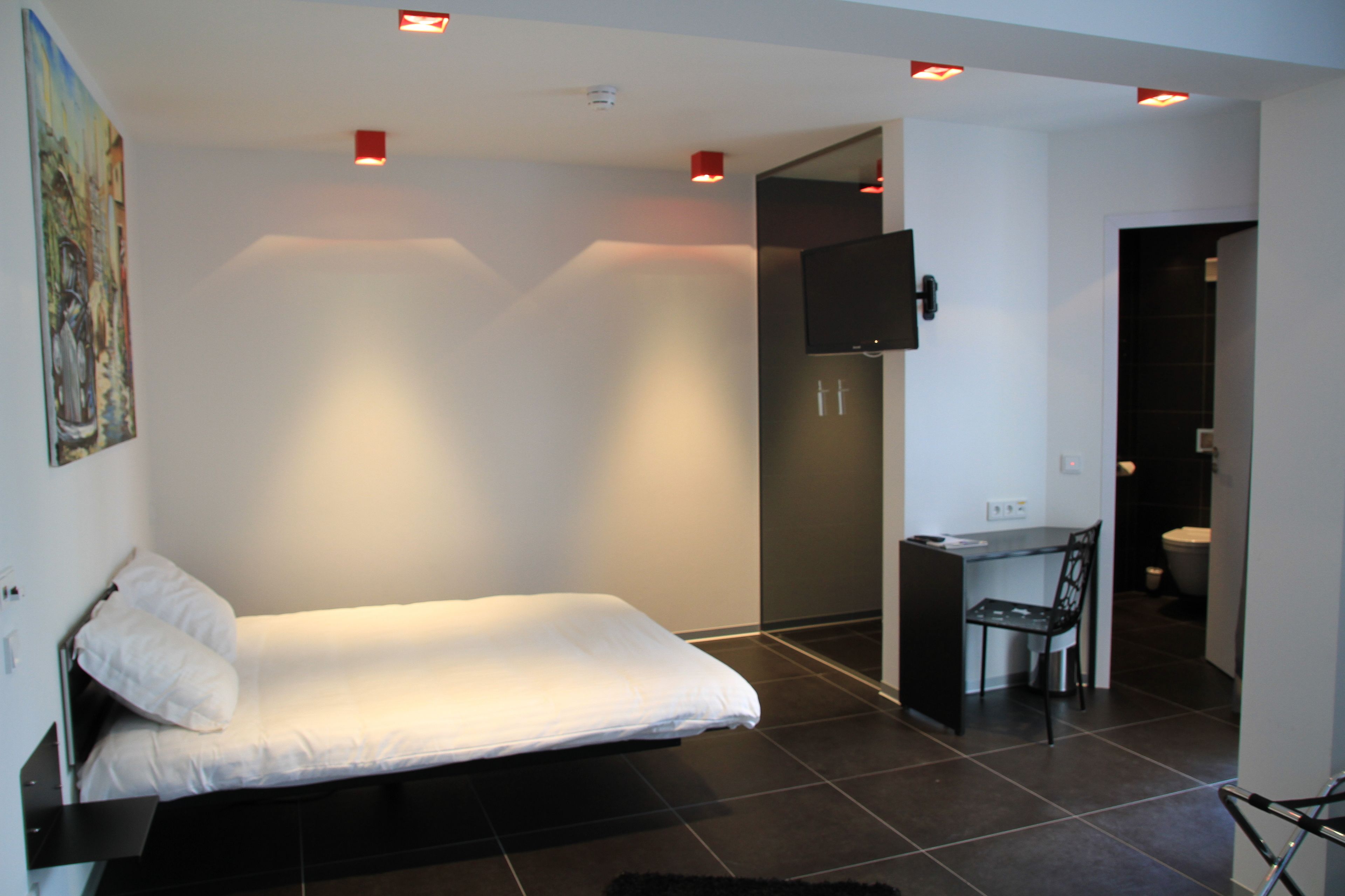 A modern bedroom with a single bed, a desk, and a chair, and a small kitchenette area.
