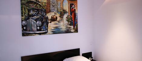 Un dormitorio con cama, mesita de noche y un cuadro en la pared.