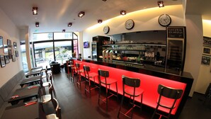 A bar area with a red counter, multiple stools, and a clock on the wall. - Hotel Grey (Luxembourg City)