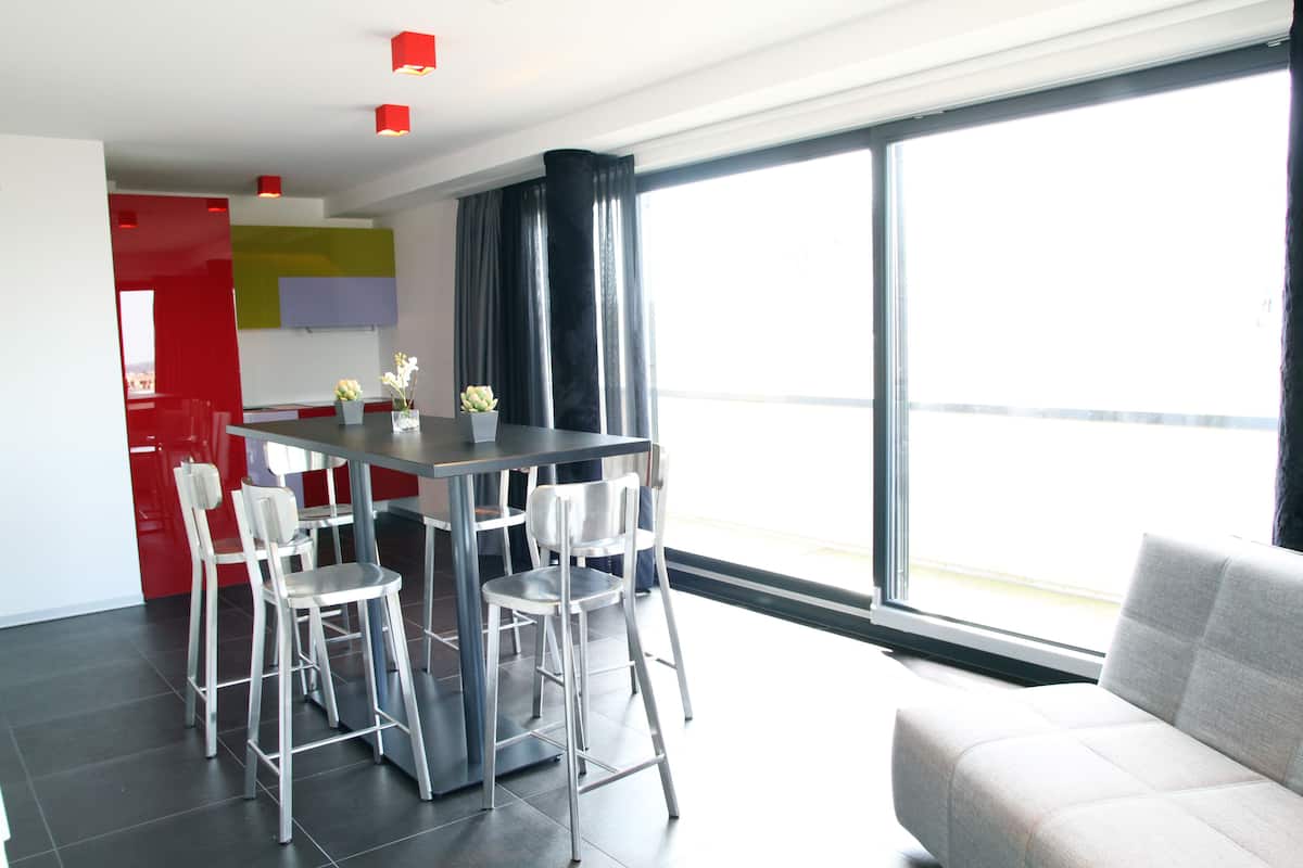 A modern living space with a dining area, a sofa, and a large window offering a view.