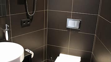 Uma casa de banho moderna com uma sanita, uma pia branca e um chuveiro com chuveiro manual.