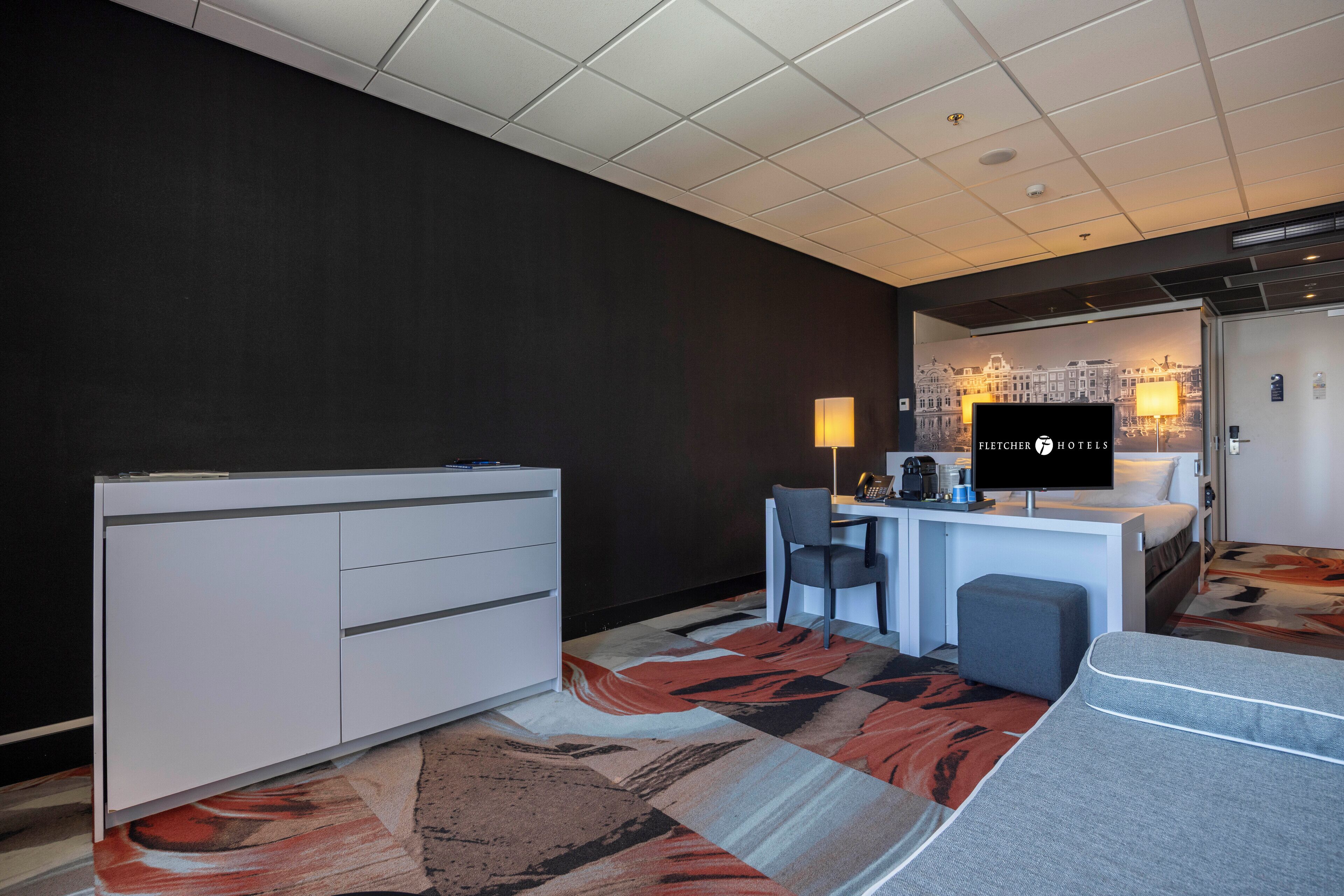 A hotel room with a bed, desk, chair, and a television.